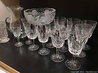 Wide view showing 10 Waterford stemmed wine/water glasses arranged in front of the etched pedestal bowl and pitcher on a dark surface.
