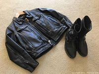 Full view of Harley Davidson women's black leather jacket laid out flat with black boots alongside on carpeted floor