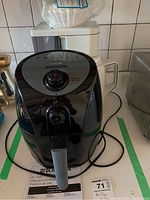 Front view of the Proctor Silex black air fryer placed on a kitchen counter with a white coffee maker behind it.