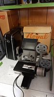 Photo showing Canon Super 8 camera, black carrying case, vintage reel-to-reel projector and original Royal box on shelf.