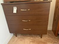 Front view of three-drawer wooden chest with metal handles and visible scratches.