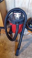 Full view of Craftsman red and black wet/dry vacuum with hose attached and nozzle resting on the drum.