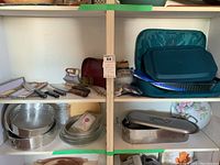 Photo showing shelves with Japanese vegetable slicers, baking pans including Pyrex with carry case, metal strainers, and kitchen tools.