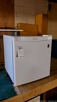 Front and side view of the white Danby bar fridge on wooden surface in basement storage area.