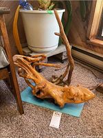 Two decorative driftwood pieces placed on a carpeted floor next to a chair and a plant pot to show overall size and form.