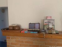 Wide view showing game items arranged on mantle including backgammon, dominos, wooden containers, playing cards, and automatic card shuffler in box.