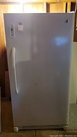 Full front view of white GE upright freezer in basement
