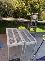 Photo showing two beige plastic shelves with vented tops outdoors on a patio with a wooden table and wooden ladder behind.