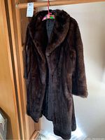 Full view of long dark brown mink coat with plush fur hanging on rack.