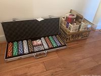 Opened aluminum poker case showing neatly arranged multi-color poker chips, two decks of cards, dealer button, and dice.