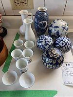 Photo showing the entire lot including saki pitchers, cups, blue and white vase, and four decorative orbs with floral and geometric patterns.