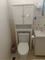 Full view of shelf installed over toilet in bathroom showing the cabinet doors, open shelf, and legs standing on floor.