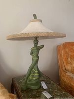 Front view of green figural lamp with white fabric shade on marble-top table