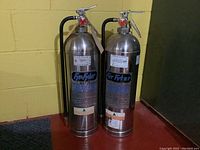 Two Fyr-Fyter metal water fire extinguishers standing side by side, showing overall physical condition and metal bodies.