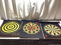 Three magnetic dartboards displayed side-by-side on a black surface shown with magnetic darts inserted. Boards vary in design with distinct circular targets and scoring areas.