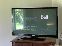 Front view of the powered-on 43-inch Samsung plasma TV displaying Bell satellite menu screen, placed on wooden TV stand with remote on stand.