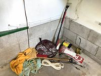 Photo showing various car tools including yellow cloth, ropes, brushes, and metal rod with handle against a concrete wall corner.