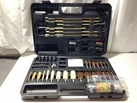 Open black hard plastic case displaying organized firearm cleaning tools including brass rods, brushes, and attachments. Some oil residue visible.