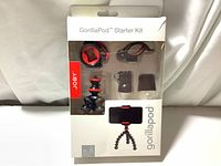 Front view of open box showing GorillaPod Starter Kit with flexible legs tripod and mounts inside clear molded plastic compartments.