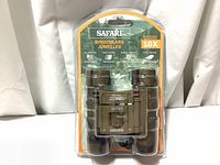 Front view of Safari 10x25 binoculars in original plastic blister packaging with cardboard backing showing product details like magnification, fully coated optics and field of view.