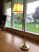 Full view of vintage brass floor lamp with pleated shade and adjustable reading arm near window with outdoor view.