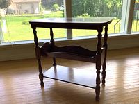 Full view of vintage solid wood three-tier side table showing turned legs and top surface with natural wood grain under daylight near window.