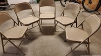 Photo showing five beige folding lawn chairs arranged in a semi-circle on a concrete floor, highlighting the full set and condition.
