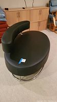 Front angled view of oval black microfiber lovers' seat with curved backrest and steel frame base.