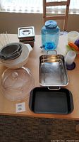 Various casserole dishes, plastic beverage dispenser, storage containers, and colander on table.