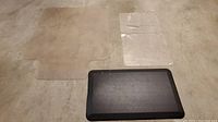 Two mats on floor: transparent chair mat with lip, and black foam pad with textured surface.