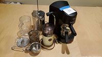 Wide view of all coffee and tea items on table including Krups cappuccino machine, French press, grinder, tea infuser, and strainers