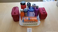 Photo of all items in the lot neatly arranged on a table with lunch boxes, bottles, sushi roller, and ice cube maker