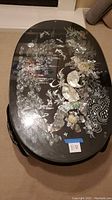Overhead angled view of the oval coffee table showcasing the mother-of-pearl inlay artwork under glass on a black lacquer base.