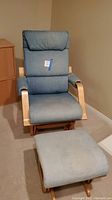 Front view of the denim upholstered rocking chair with padded arms and headrest beside matching ottoman showing upholstery and wood frame.