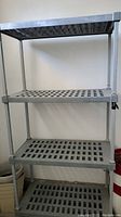 Four-tier gray metal utility shelf alone against wall, empty.