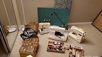 Overall view: three machines, cutting mat, totes, lamp, trays of notions