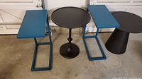 Photo showing two blue rectangular metal tables with open bases and one black round metal pedestal table