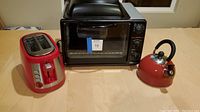 Full lot display, showing the Elite Gourmet toaster oven, red Hamilton Beach 2-slice toaster, and red Euro-ware kettle on a wooden surface.