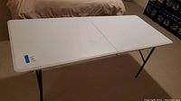 Full view of white folding table showing the top surface, clean and rectangular with leg supports underneath.