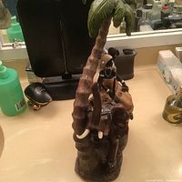 Photo of figurine showing front and side view including the elephant, couple and palm tree on a flat surface