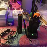 Arcshell walkie-talkie on charger with flashlight and earphones laid out on a pink surface.