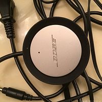 Close-up of circular Bose control pod, showing Bose logo on silver top and attached cables.