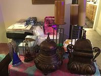 Image showing a variety of candle holders and decorative containers on a table including stained glass, metal candle holders with candles, a brass lidded container, and a small metal box.