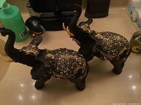 Pair of large black elephant figurines, covered with detailed gold decorative patterns on backs and headpieces, shown from side angle.