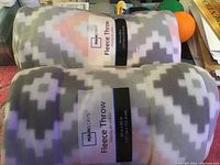 Two rolled fleece throws with black bands labeled Mainstays Fleece Throw, geometric pattern visible.