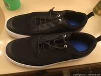 Pair of black Maui and Sons sneakers with white soles shown side-by-side on surface.