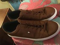 Side view of brown leather Tommy Hilfiger sneakers with white sole and lace-up closures, showing logo on side.