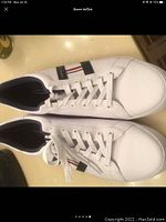 Top view of white Tommy Hilfiger sneakers with lace up tops, black interior lining, and signature side stripe with branding.
