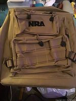 Front view of tan nylon backpack with two zippered front pockets and black embroidered NRA logo