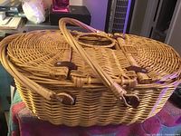 Side view showing the wicker weave, curved handles and flaps of the picnic basket.